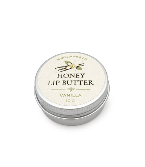 A round silver metal tin of Banksia Hive Co. Honey Lip Butter in Vanilla, featuring a cream-colored label with green vanilla leaf and bean illustrations.